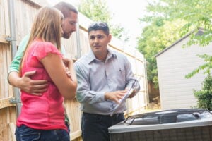 Technician explaining furnace maintenance details to a couple next to an outdoor unit.