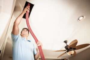 Technician performing air duct cleaning using a large vacuum hose in a residential ceiling vent.